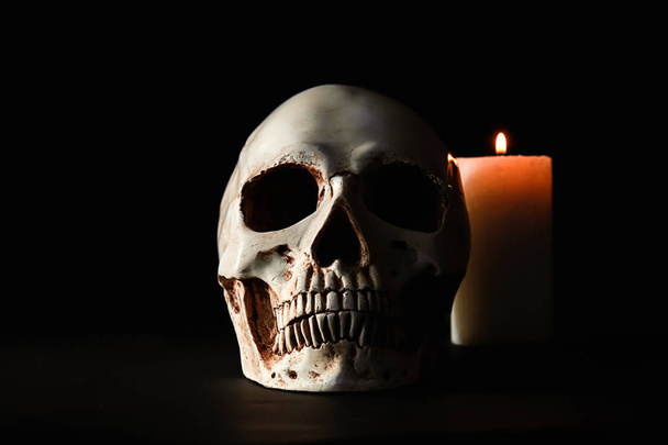 Human skull and burning candle on black background - Foto, afbeelding