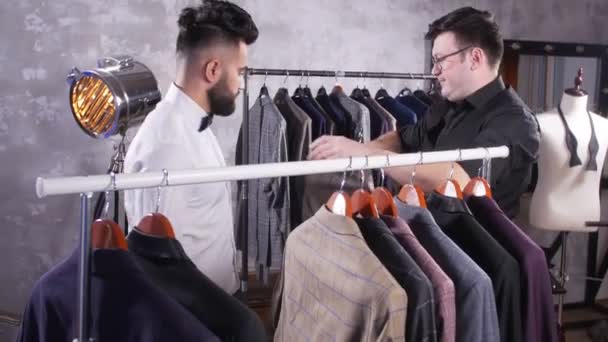 Concetto di shopping. Venditore aiuta un giovane uomo a scegliere un abito nel negozio
 - Filmati, video