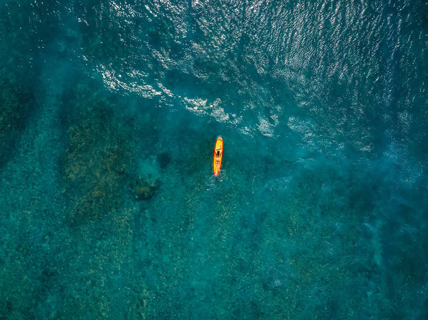 Сёрфер женщина в тропическом океане ждет волну у желтой доски для серфинга. Вид с воздуха
. - Фото, изображение