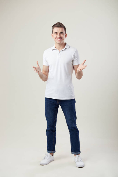 Joyful guy dressed in a white t-shirt and jeans stand in the studio on a white background - Photo, image