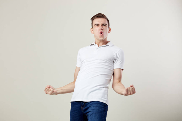 Full of energy joyful guy dressed in a white t-shirt and jeans happily shouts in the studio on a white background - 写真・画像