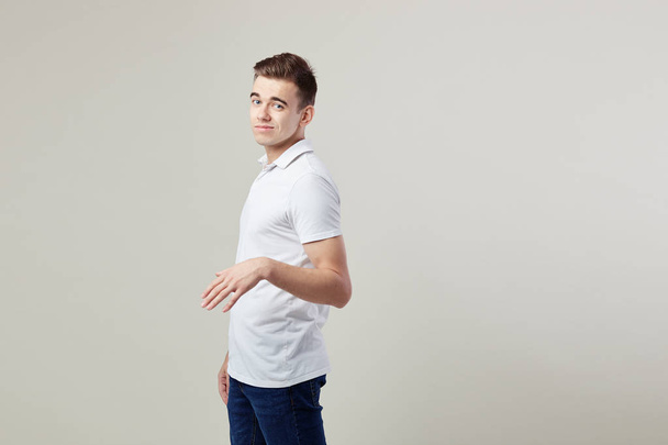 Indifferent  guy dressed in a white t-shirt and jeans is on a white background in the studio - Photo, image