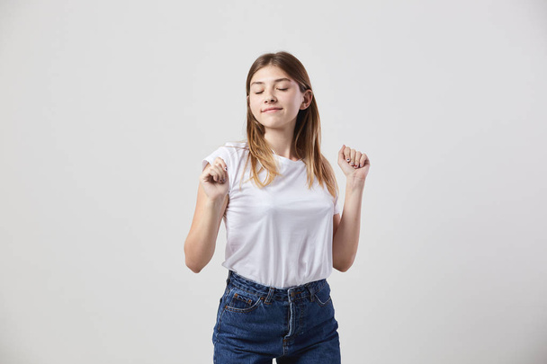 Calm and happy girl dressed in a white t-shirt and jeans is on a white background in the studio - Photo, image