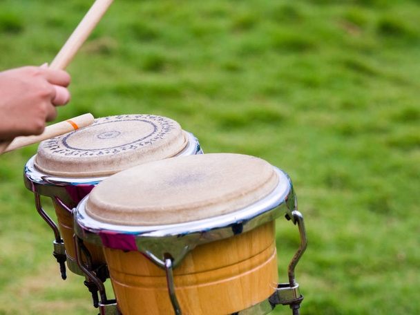 Close-up van drummer handen bespelen van percussie Bongo drums met drumsticks in de groene natuur achtergrond. - Foto, afbeelding