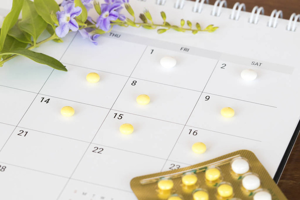 geboortebeperking pillen anticonceptiva vrouw voor niet wilt hebben van baby- en kalender voor plan met paarse bloemen decoratie plat lag stijl op witte achtergrond  - Foto, afbeelding