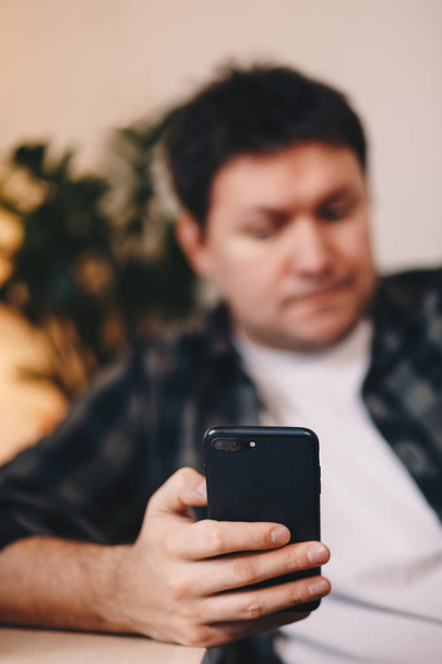 Close-up detail van een jonge man hand met behulp van een mobiele telefoon, typen zittend in een persoonlijke werkruimte. Focus op het apparaat. - Foto, afbeelding
