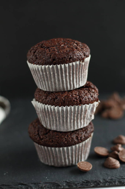 バック グラウンドでチョコレート ・ ドロップで黒い背景にチョコレートの自家製カップケーキ マフィン。パン屋さんのスタイル。暗い食品写真縦 - 写真・画像