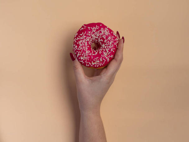 Mão de mulher segurando donut em fundo de pêssego. Deitado plano mínimo, conceito de vista superior
. - Foto, Imagem