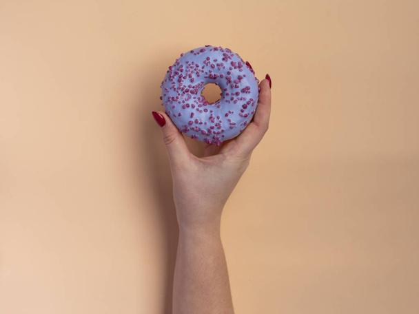 Women's hand holding donut on peach background. Minimal flat lay, top view concept. - Fotoğraf, Görsel