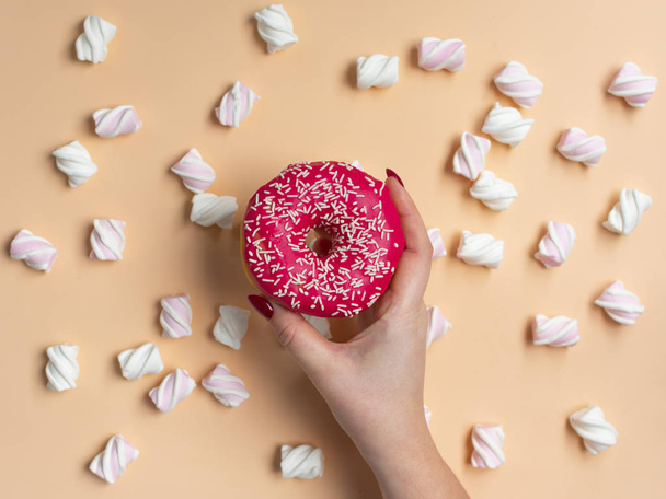 Women's hand hebt donut met marshmallow op perzik achtergrond - Foto, afbeelding