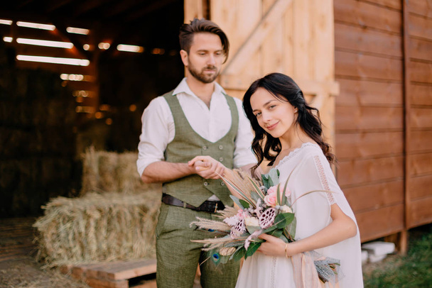 groom holds bride by hand while standing on ranch on sunny day - Foto, imagen