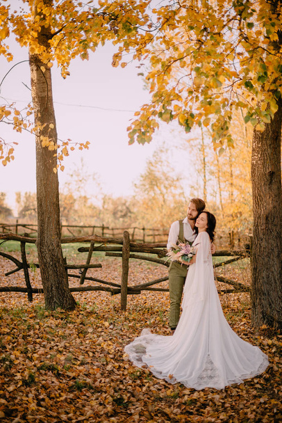 Groom embraces bride among the autumn foliage - Foto, Imagen