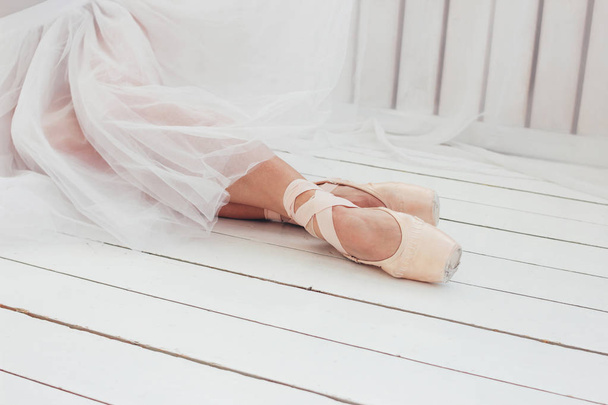Young woman authentic ballerina ballet dancer in pointe shous sitting on white floor - Foto, Imagen