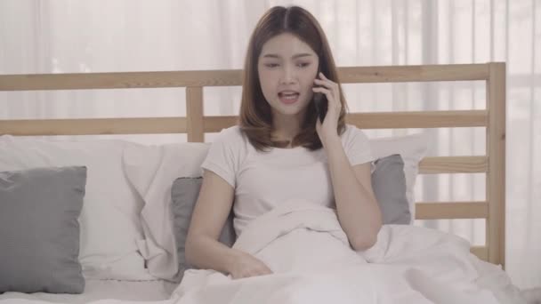 Mladá asijská žena pomocí smartphone vleže na posteli po probuzení ráno, krásné atraktivní japonská dívka s úsměvem odpočívat v pokoji doma. Dámská domácí koncept času se těší. - Záběry, video