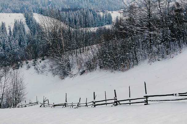 Dřevěný plot pokrytý sněhu cap. Zimní venkovské krajiny, vesnice nebo farma, zasněžené vrcholky hor a lesů v pozadí - Fotografie, Obrázek