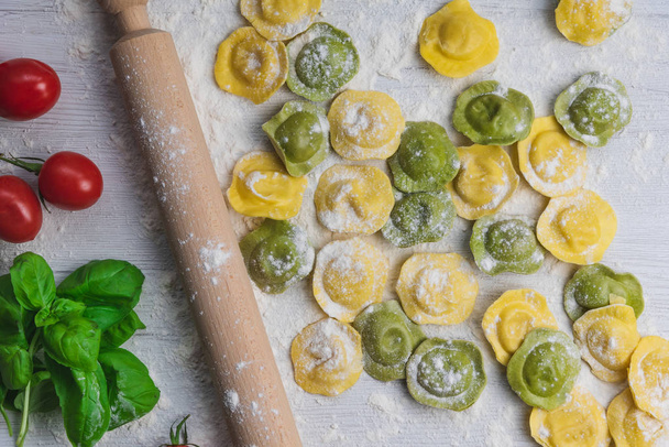 自家製の新鮮なイタリアのラビオリ パスタ小麦粉、バジル、トマト、背景、上面の白い木製テーブルの上. - 写真・画像