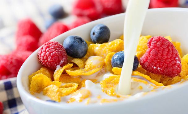 Pouring milk into bowl of Corn Flakes with berries - Photo, Image