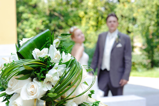 Beautiful wedding bouquet and newlyweds in the background. - Valokuva, kuva