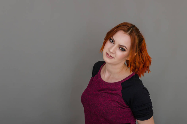 Portrait of a beautiful woman with red hair in a t-shirt posing on dark gray background turned sideways. Women's health, beauty, style - Fotoğraf, Görsel