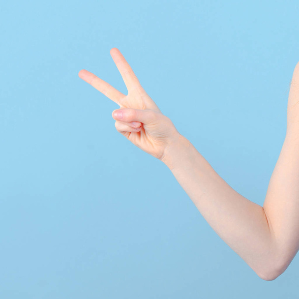 Female hand shows two fingers on blue background. Peace and victory - Foto, Bild