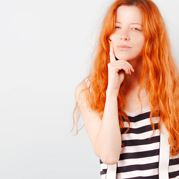 Redhead girl squints and frowns. Doubt, choice and suspicion. Emotions and lifestyle - Фото, изображение