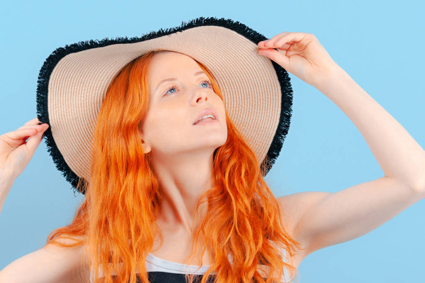 Red-haired girl holds hands straw hat and looks up. Dreams of relaxing on beach. Emotions and lifestyle - Fotografie, Obrázek