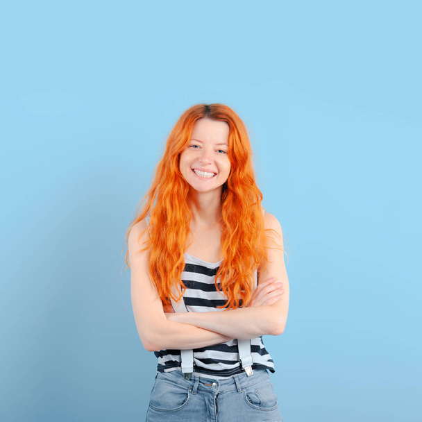 Red-haired girl smiles, having combined hands on breast on blue background. Positive and approval - Fotoğraf, Görsel