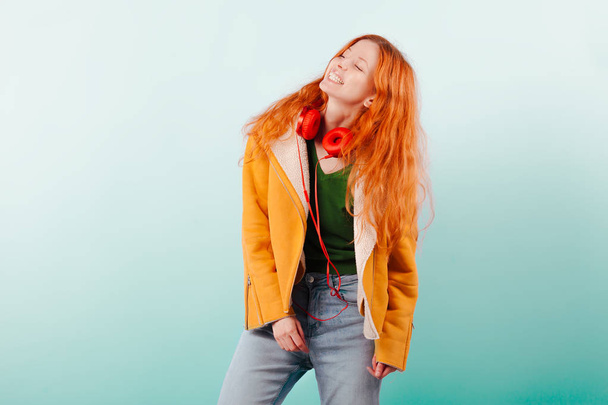 Red-haired girl in red headphones and yellow jacket laughs. Positive, happiness, joy and pleasure. Emotions and lifestyle - Fotografie, Obrázek