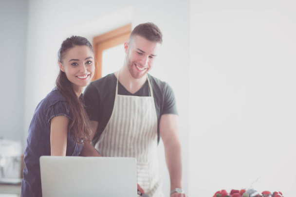 Junger Mann schneidet Gemüse und Frau steht mit Laptop in der Küche - Foto, Bild