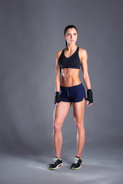 Muscular young woman posing in sportswear against black background. - 写真・画像