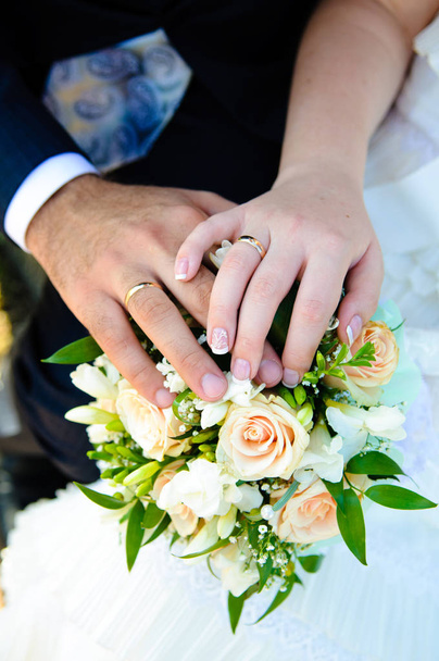 Hands of newlyweds with wedding rings on a bouquet of the bride. - Photo, Image