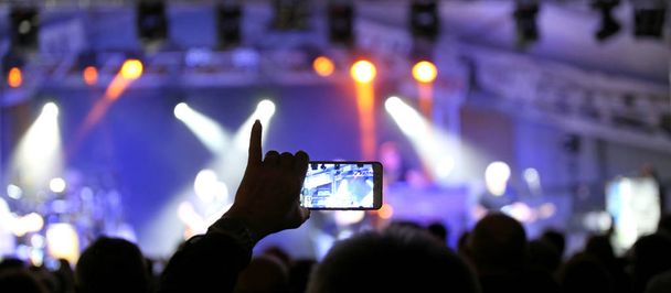 pessoa com a mão rosada levantada enquanto fotografa o concerto de rock usando um smartphone moderno
 - Foto, Imagem
