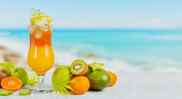 Καλοκαιρινό κοκτέιλ με διάφορα τροπικά φρούτα γύρω. Μήλο, ακτινίδιο, μανταρίνι, πορτοκάλι, μάνγκο, καράμβολες. Γυαλί πορτοκαλί ποτό με θολούρα παραλία στο παρασκήνιο - Φωτογραφία, εικόνα