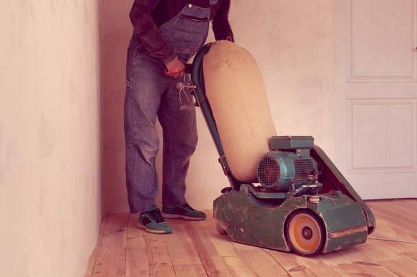 Carpenter polírozza a fából készült padló, elektromos csiszoló Faipari gép egy szobában - Fotó, kép