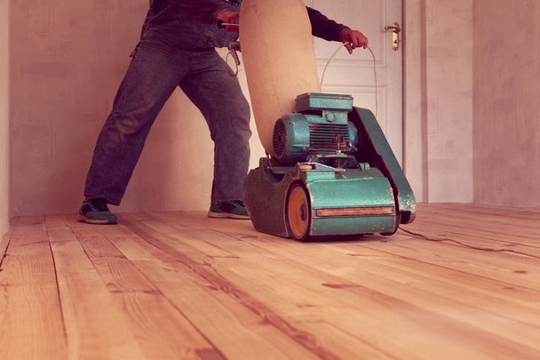 плотник полирует деревянный пол электрошлифовальной машиной в помещении
 - Фото, изображение