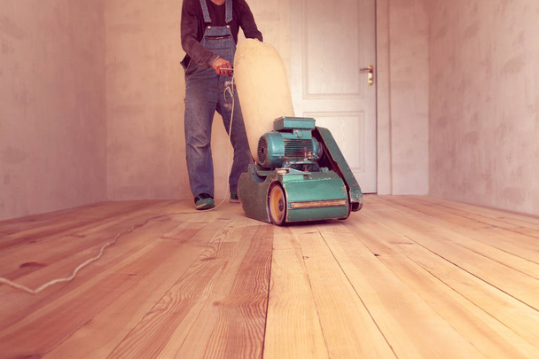 carpintero pule un piso de madera por la máquina de madera de molienda eléctrica en una habitación
 - Foto, imagen