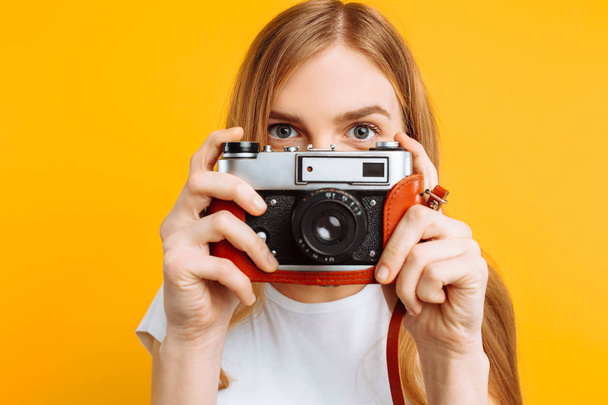 beautiful girl with a camera in her hands, on a yellow background, a woman takes pictures - Foto, Imagem