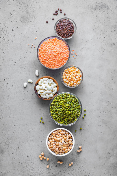 Assortment of colorful legumes in bowls, lentils,  kidney beans, chickpeas, mung, peas on grey background, top view, copy space. Healthy food, dieting, nutrition concept, vegan protein source. - Фото, изображение