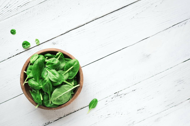Baby spinach leaves in bowl on white wooden background, top view, copy space. Clean eating, detox, diet food ingredient - green organic spinach. - Fotó, kép
