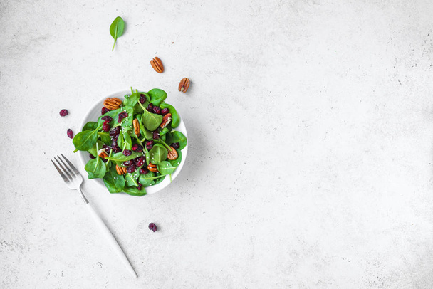 Spinach salad with  pecan nuts and dry cranberries on white background, copy space. Heathy clean vegan raw food, fresh salad. - Foto, imagen