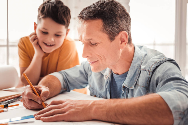 Dark-haired father drawing geometrical figures along with his adopted child - Photo, image