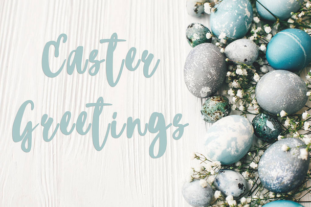 Easter Greetings text sign on stylish easter eggs with spring flowers on white wooden table - Fotó, kép