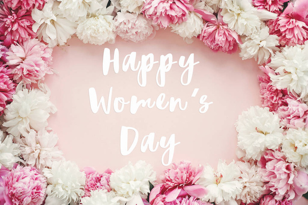 Happy Women 's Day text sign on stylish peonies flat lay. Розовые и белые пионы обрамляются розовой бумагой
 - Фото, изображение