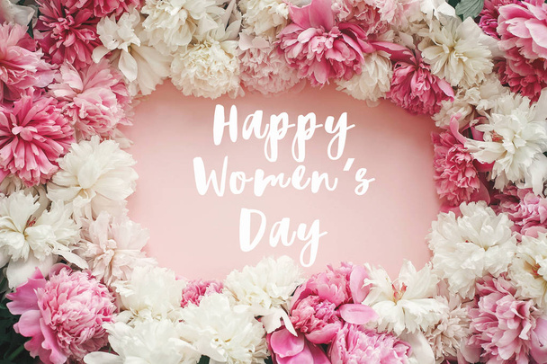 Cartel de texto del Día de la Mujer feliz en peonías elegantes acostado plano. Marco de peonías rosadas y blancas sobre papel rosa pastel
 - Foto, imagen