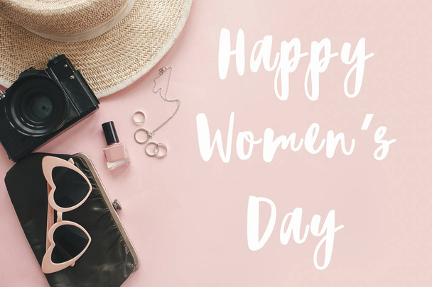 Happy Women 's Day text sign at stylish girly photo camera, retro sunglasses, jewelry, hat on pastel pink paper
 - Фото, изображение