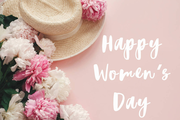 fröhliches Textschild zum Frauentag am Strohhut mit weißen und rosa Pfingstrosen auf pastellrosa Papier - Foto, Bild