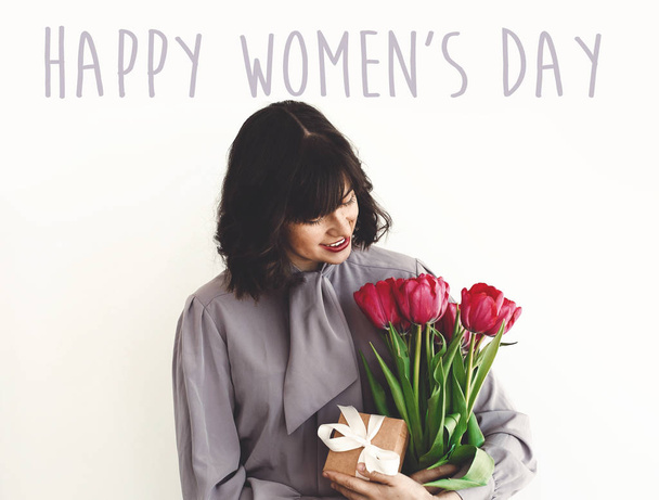 Felice giorno delle donne segno di testo e bella ragazza che tiene elegante bouquet di tulipani e scatola regalo su sfondo bianco
 - Foto, immagini