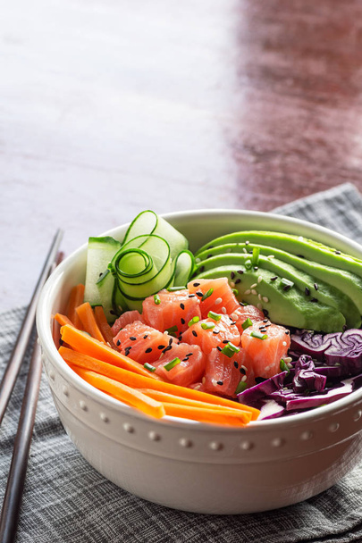 Hawaiian Poke Bowl with Sliced Salmon, Avocado, Cucumber, Carrot, and Purple Cabbage over Brown Rice with Chopsticks and Copy Space in Background - Fotoğraf, Görsel