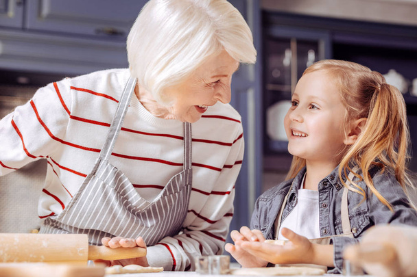 Pretty girl smiling to her granny while making cookies with her - Foto, Bild