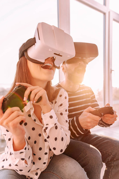 Happy boyfriend and girlfriend wearing VR glasses holding gamepads - Photo, image